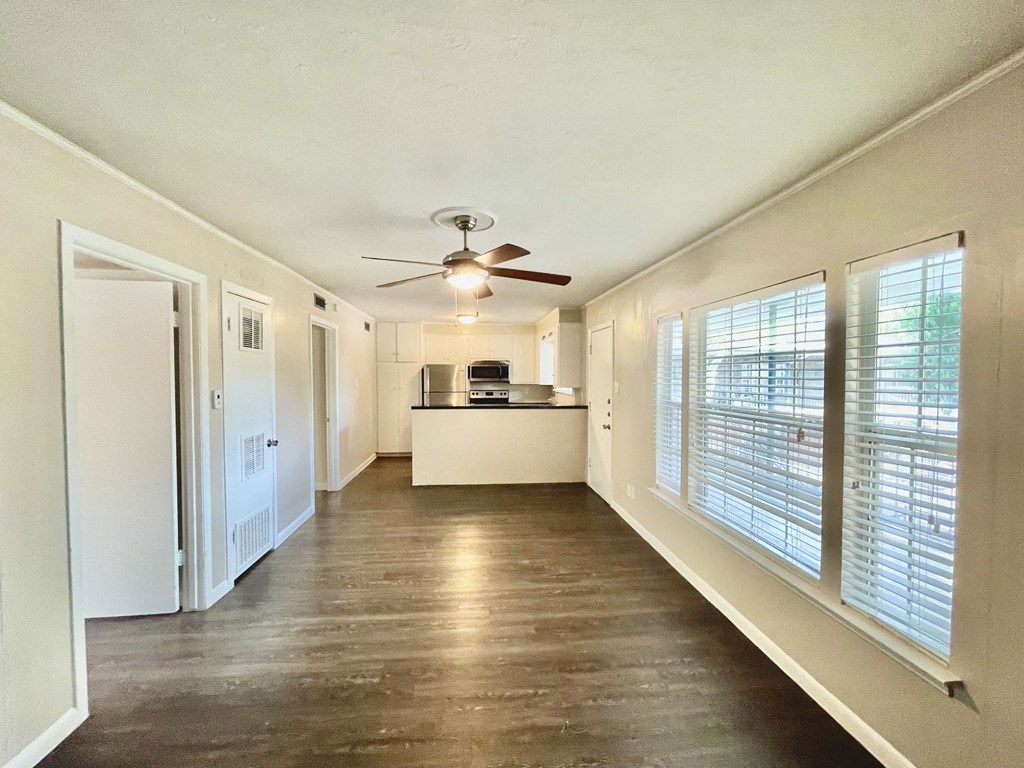 an empty living room with a ceiling fan and large windows