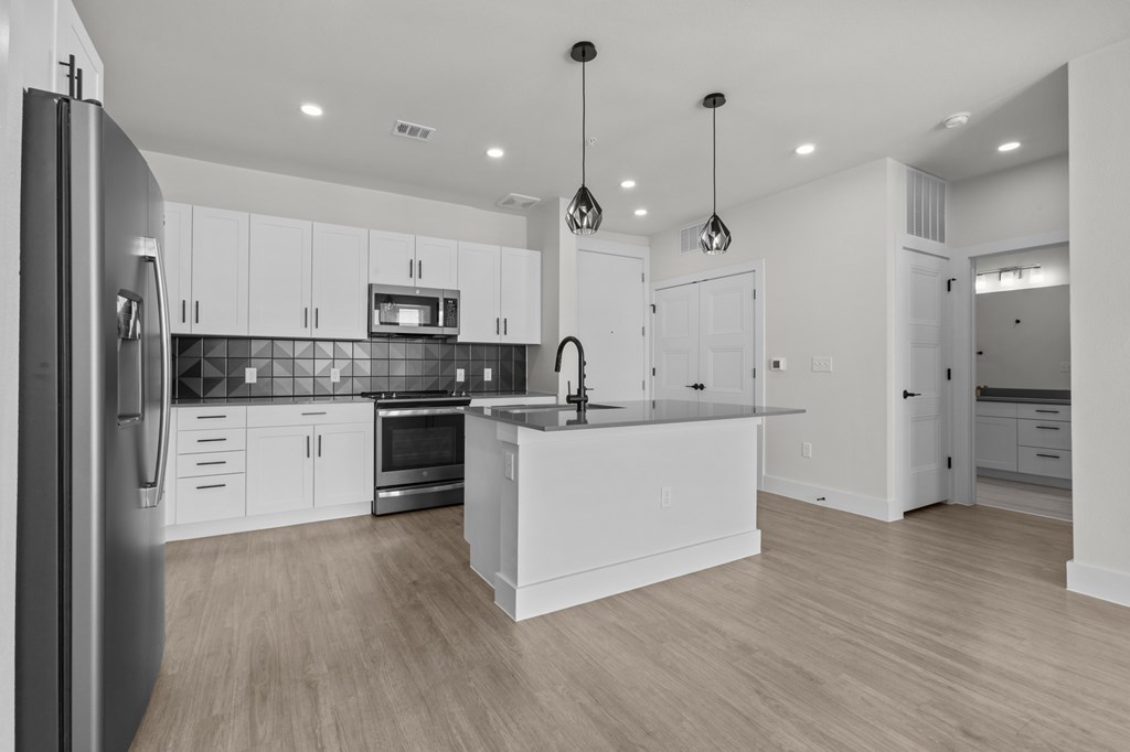 A modern kitchen with white cabinets and a wooden floor.