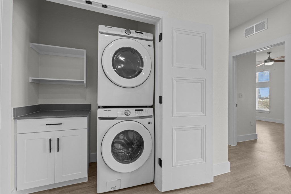 A white washing machine is in a laundry room with a cabinet and shelves.