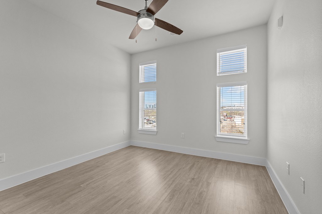 A room with a ceiling fan and two windows.