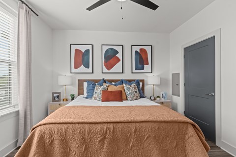 A bedroom with a bed covered in an orange blanket and three framed artworks on the wall.