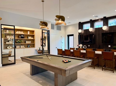 A pool table is in the middle of a room with a shelf and chairs.