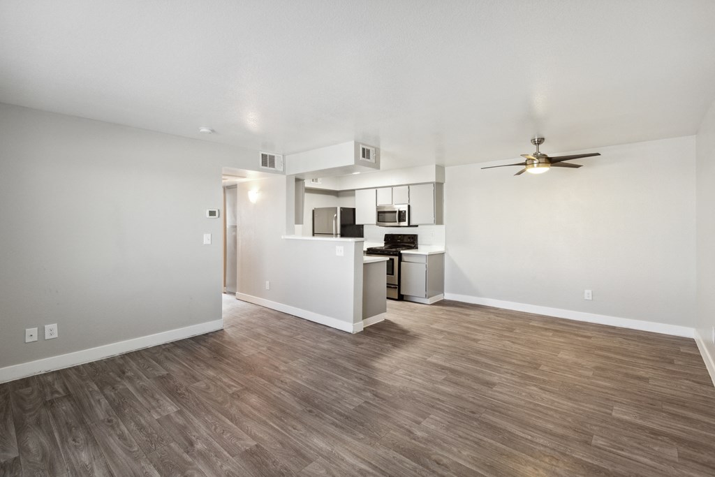 a living room with a ceiling fan and a kitchen in the background