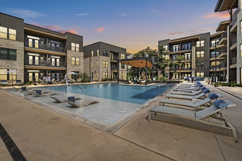 A swimming pool surrounded by sun loungers and apartment buildings.