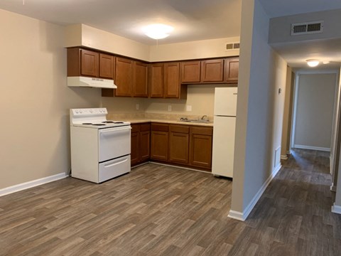 an empty kitchen with white appliances and wood flooring