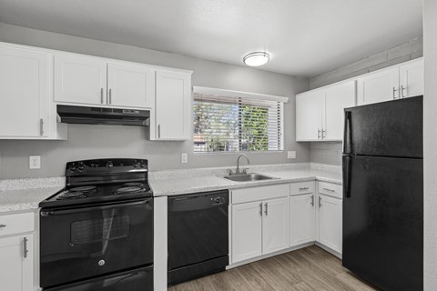 A black refrigerator sits in a kitchen with white cabinets.