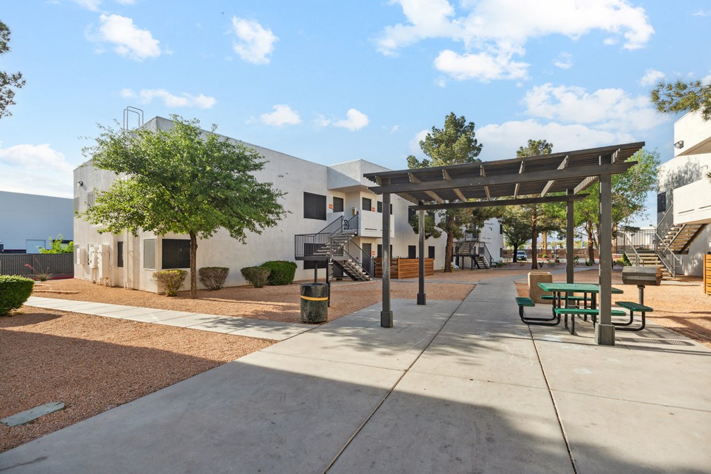 a covered area with benches and trees in front of a white building