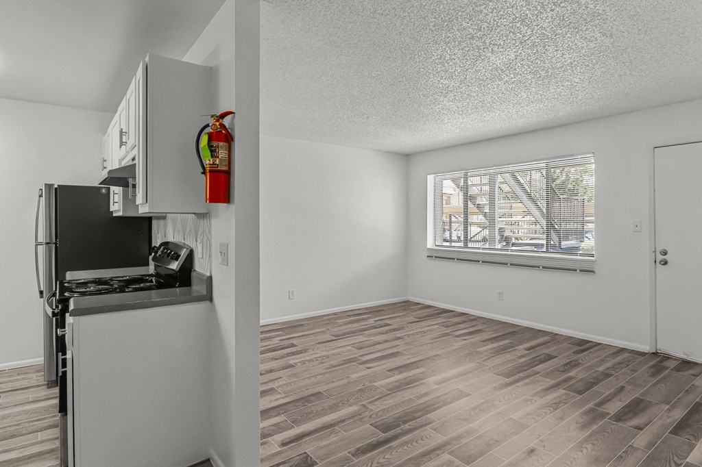 the living room and kitchen of an apartment with a refrigerator and a window