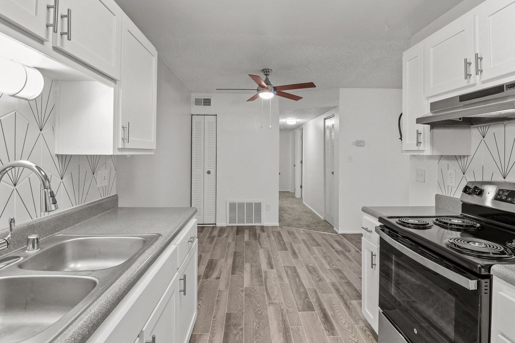 an empty kitchen with white cabinets and stainless steel appliances and a ceiling fan