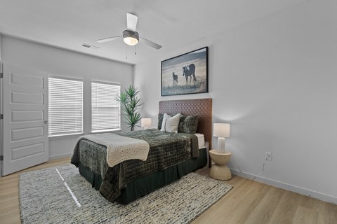 A bedroom with a bed, a rug, a fan, a painting, and a lamp.