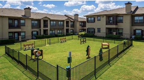 A black fence surrounds a green lawn in front of apartment buildings.
