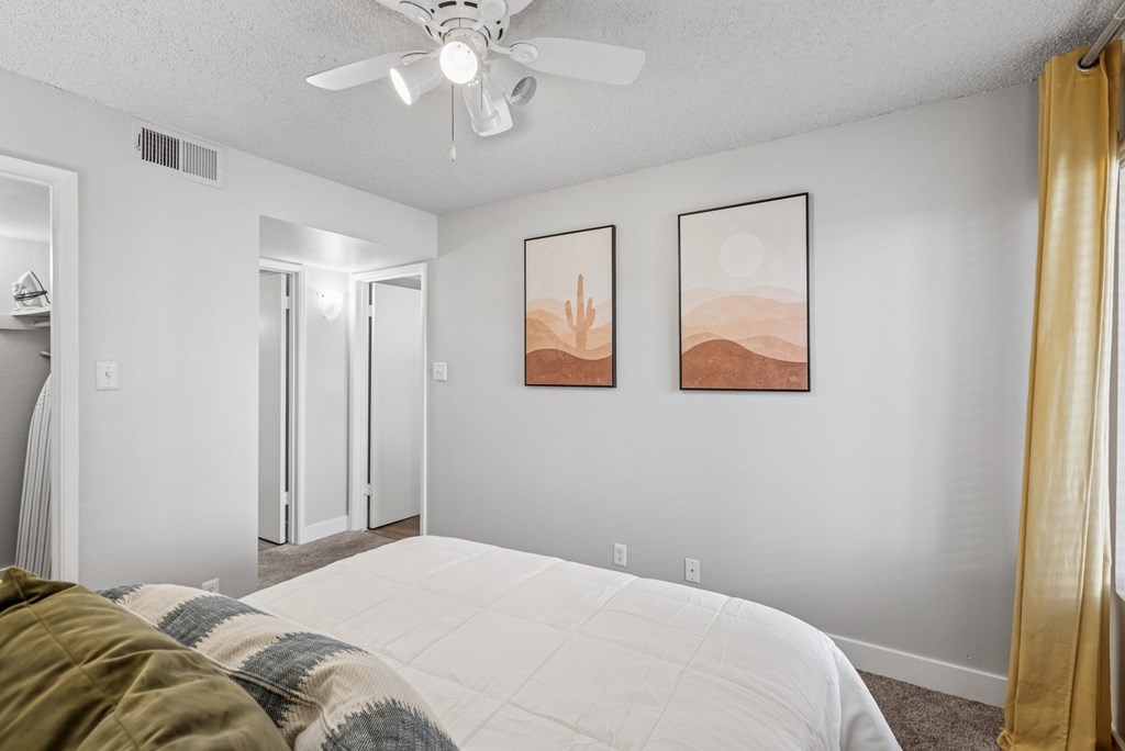 A bedroom with a bed, a ceiling fan, and two framed pictures on the wall.