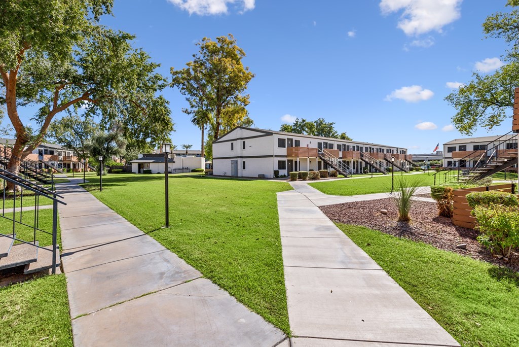 A sunny day at a park with a walking path and green grass.