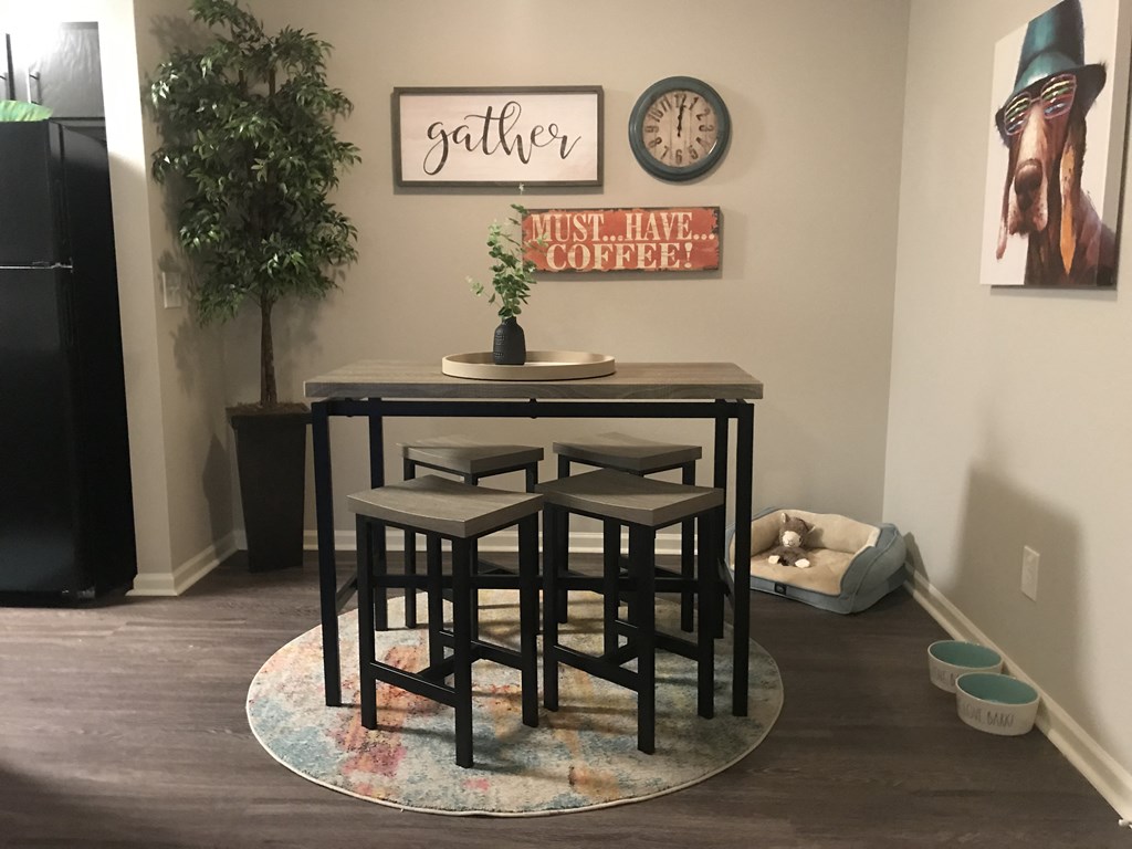a table and two stools in a room with a plant and a clock on the wall