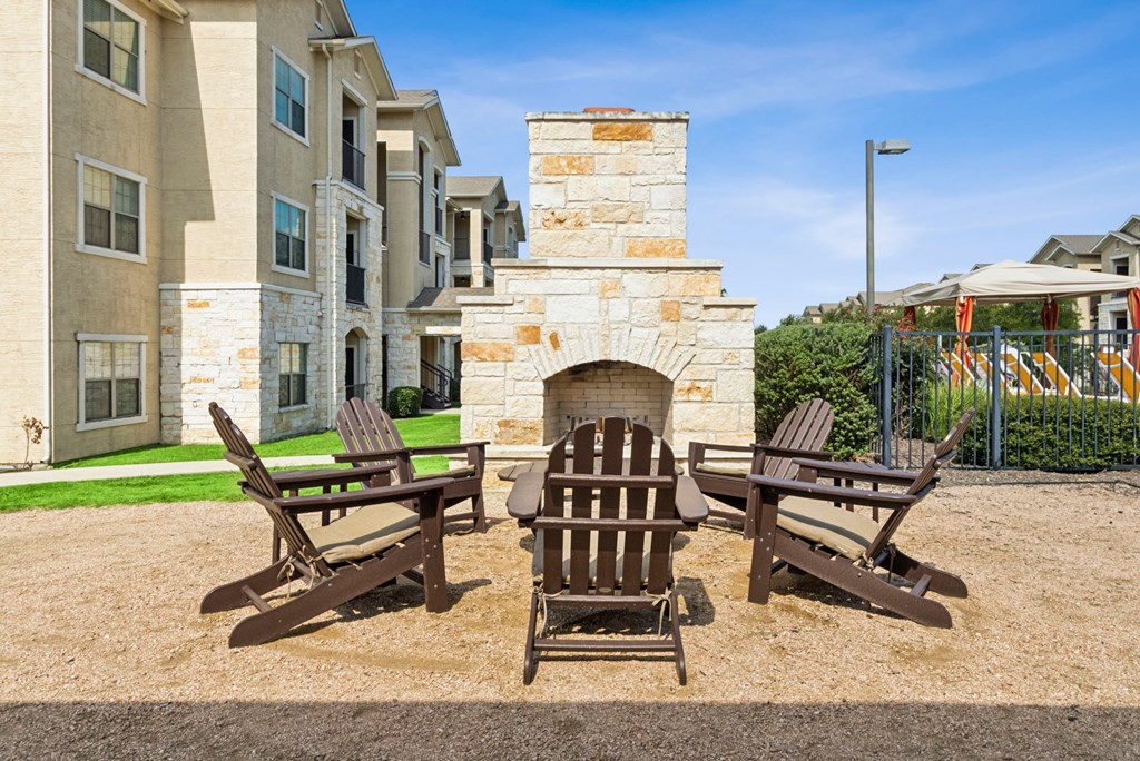 A fireplace is in the middle of three chairs on a patio.