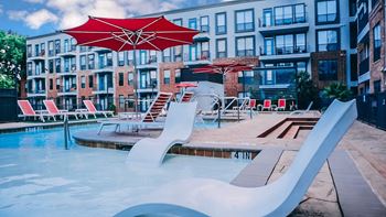 a swimming pool with chairs and umbrellas at an apartment building