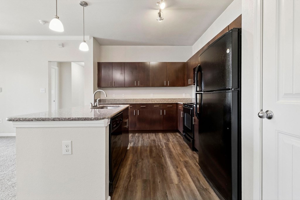 A kitchen with a black refrigerator and brown cabinets.