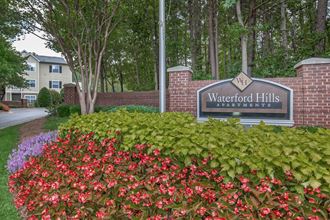 the entrance to waterford hills apartments with flowering plants and a sign