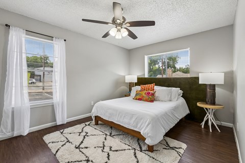 A bedroom with a bed, a ceiling fan, and a window with white curtains.