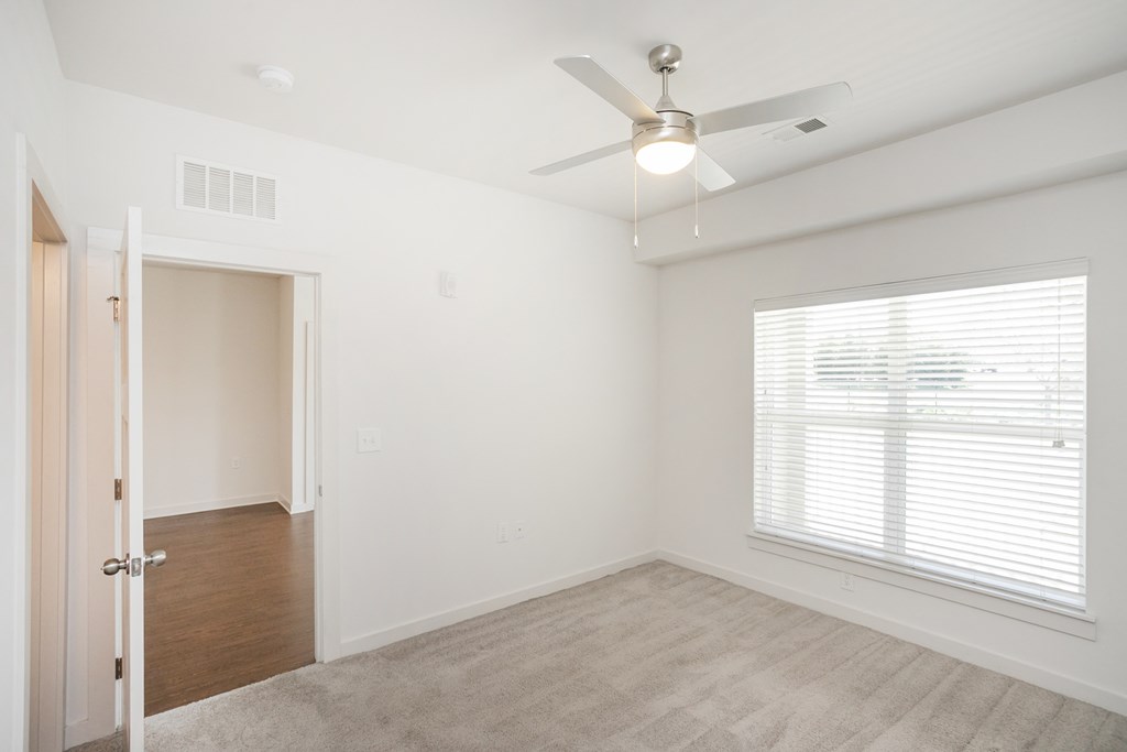 an empty bedroom with a ceiling fan and a window