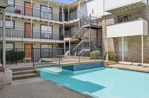 A swimming pool in front of a building with a balcony.