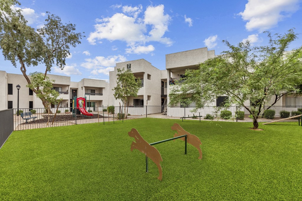 a yard with a seesaw and a dog statue in front of a building