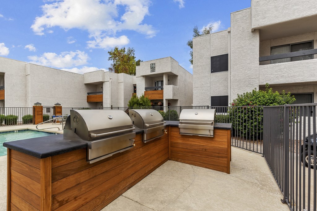 two bbq grills sit on a wooden deck in front of a pool