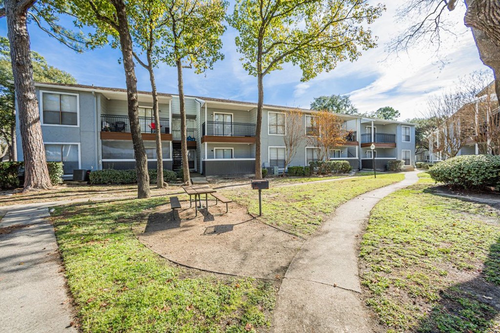 A park area with a bench and a tree in front of apartment buildings  at Cashel Springs, Houston, TX.