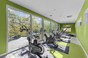A gym with exercise bikes and a view of trees outside.