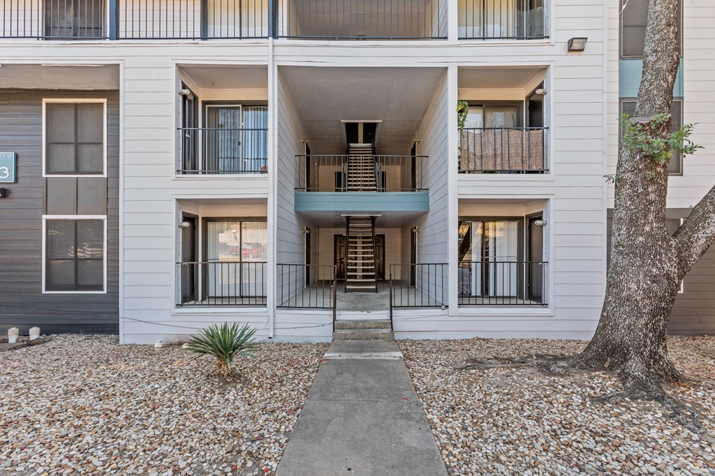 front entrance to a white building with a tree and a sidewalk