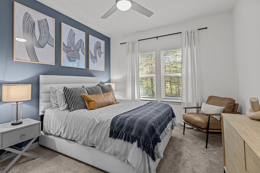 A bedroom with a bed, chair, and artwork on the wall.