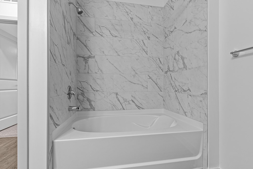 A white bathtub with a marble wall behind it.