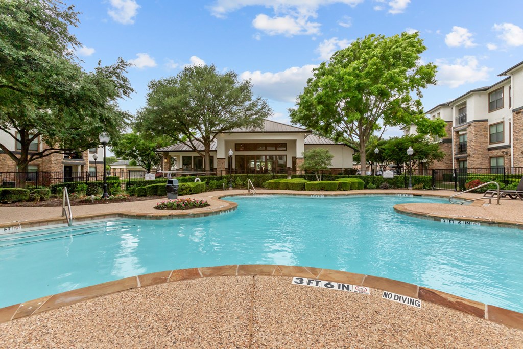 A pool surrounded by trees and a building in the background.