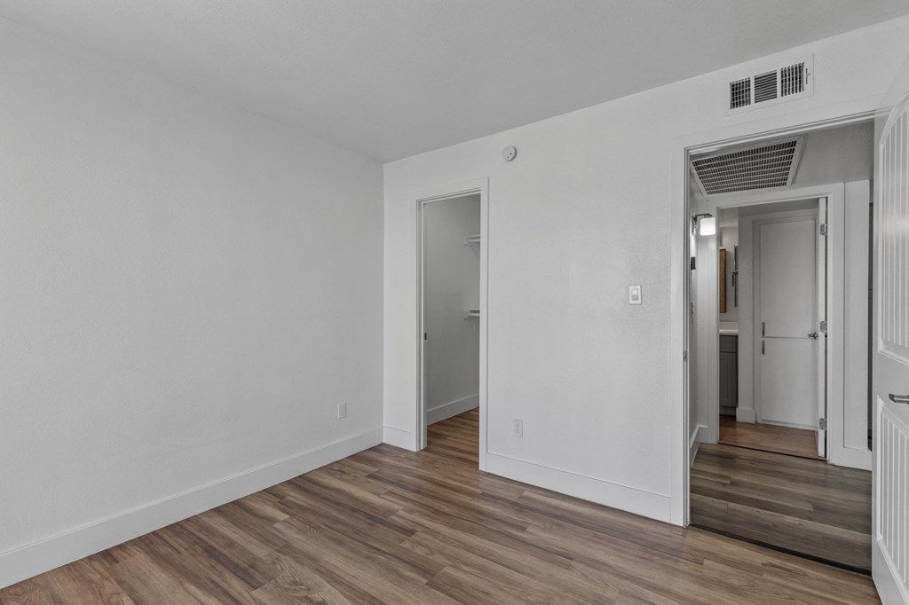 the living room of an apartment with white walls and wood flooring