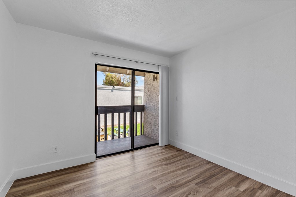 an empty living room with a sliding glass door to a balcony