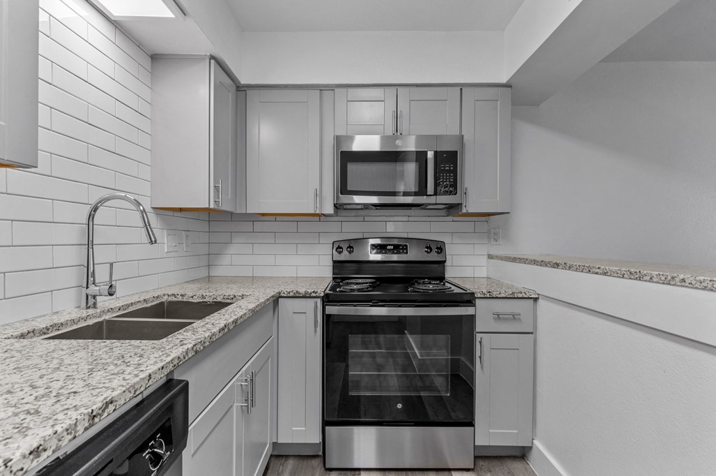 an empty kitchen with white cabinets and granite counter tops and a stove and microwave