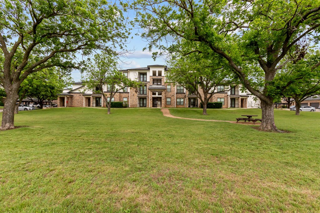 A grassy area with trees and a building in the background.