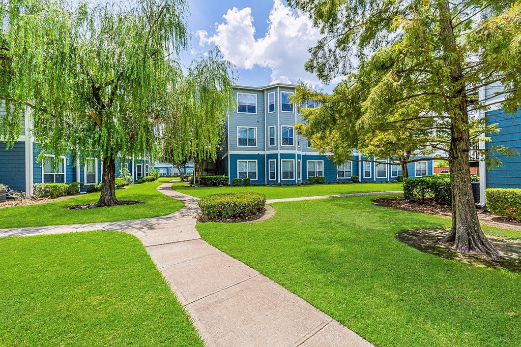 a sidewalk leading to a blue building with green grass and trees