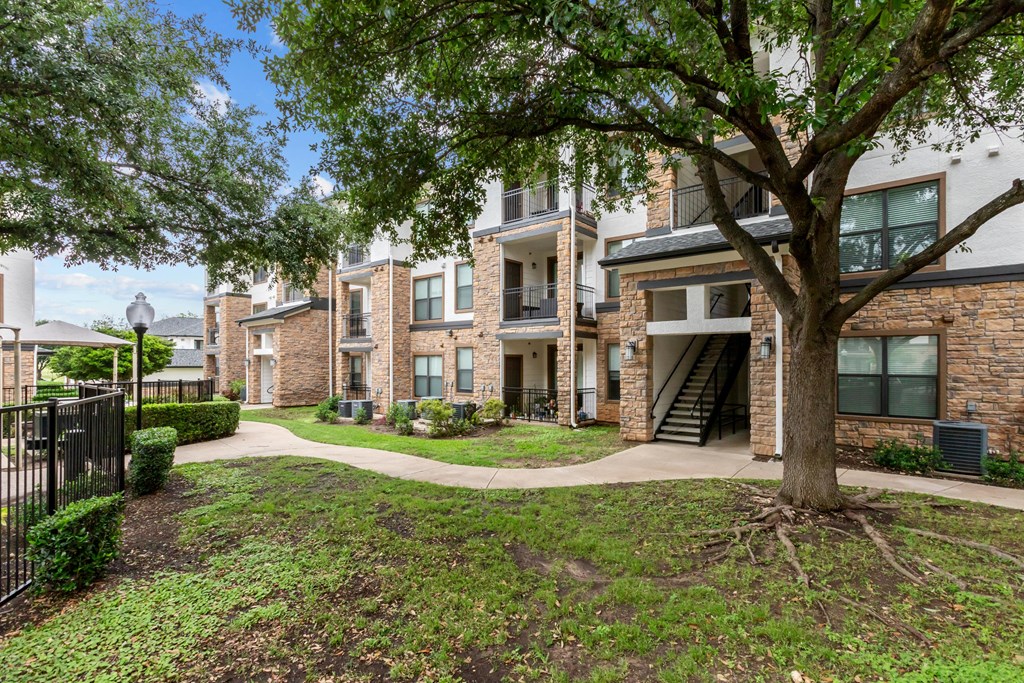 A tree in front of a building with a black fence.
