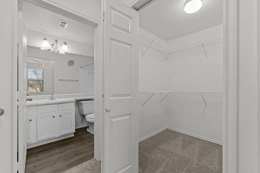 A white bathroom with a toilet, sink, and a walk-in closet.