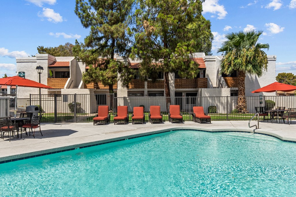 a swimming pool with red chairs and umbrellas in front of a building