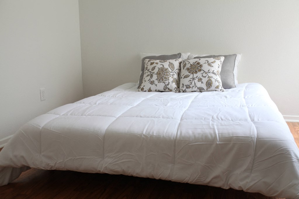 a bedroom with a white comforter and pillows on a bed