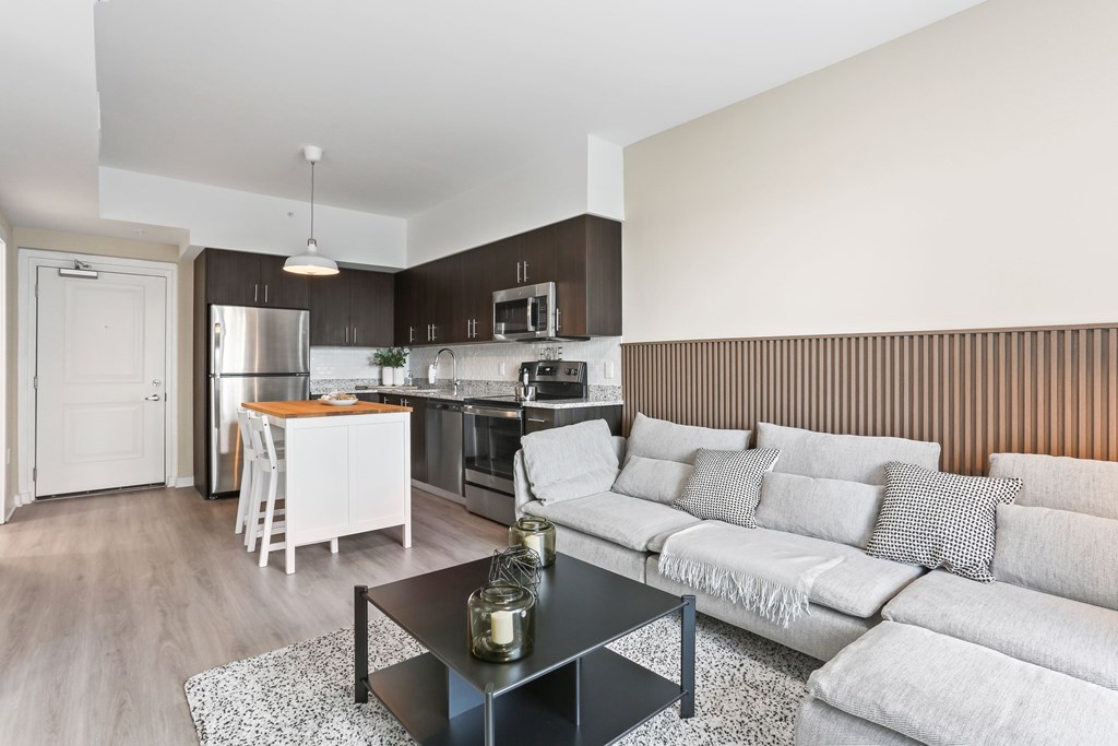 A modern kitchen with a dining table and a grey sofa.