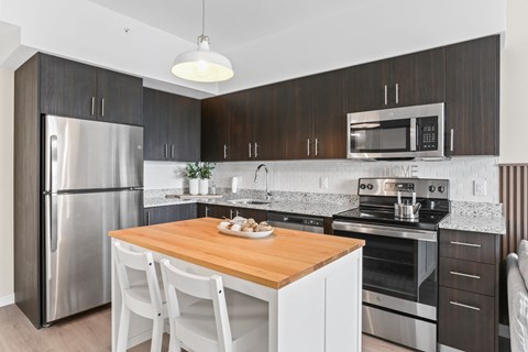 a kitchen with dark cabinets and a white island with two white chairs