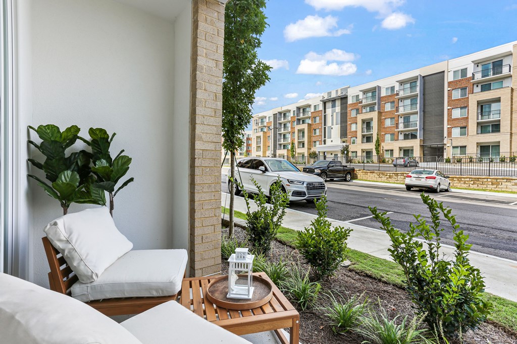 A balcony with a chair and table overlooking a street with cars and buildings.