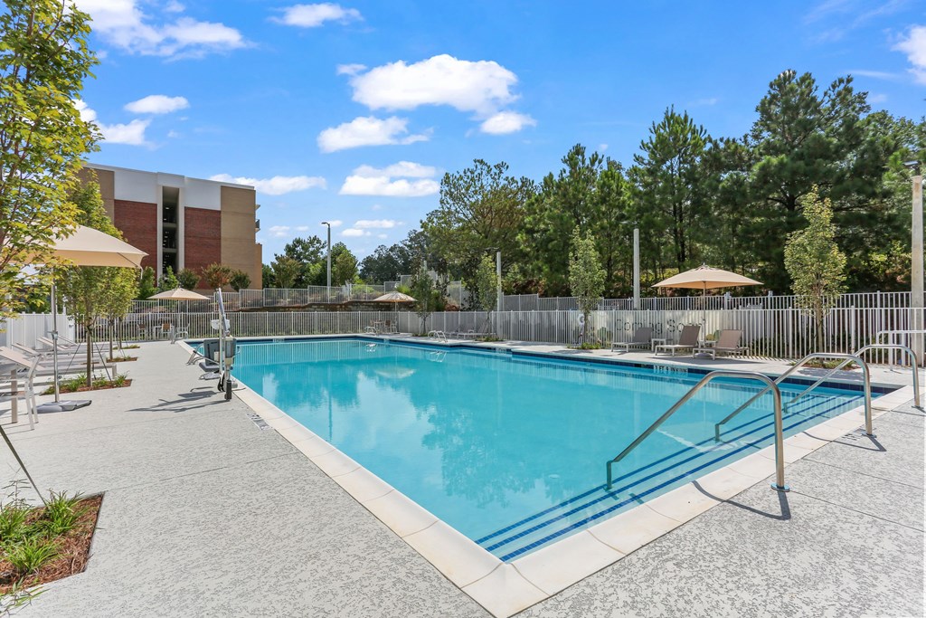 A large outdoor swimming pool surrounded by a concrete patio and a metal fence.