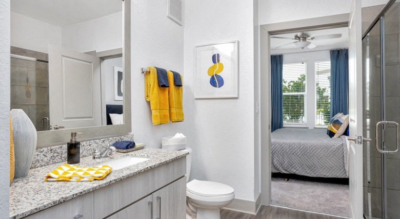 A bathroom with a white toilet, sink, and a bedroom in the background.