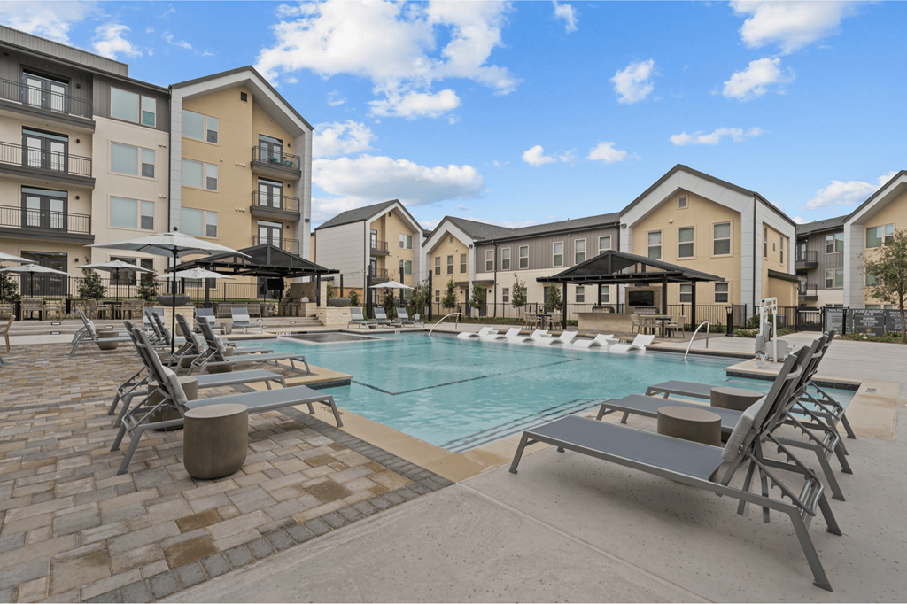 A swimming pool surrounded by sun loungers and apartment buildings.