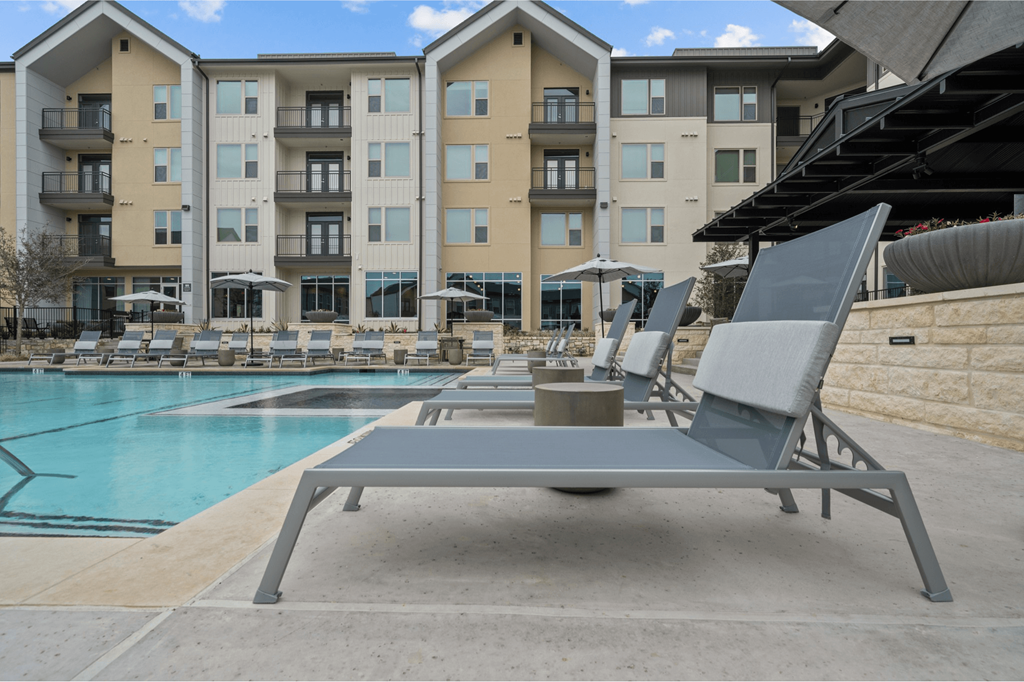 A sun lounger is in the foreground of a swimming pool.
