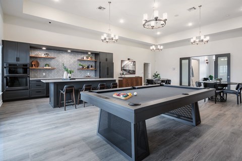 A pool table is in the middle of a room with a kitchen in the background.